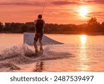 Wakeboarder making tricks. Low angle shot of man wakeboarding on a lake. Man water skiing at sunset.
